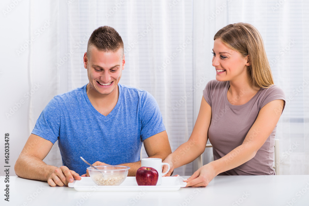 Beautiful young woman is giving breakfast to her happy husband. Beautiful young woman is giving breakfast to her happy husband.