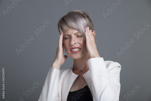 Young woman has headache, isolated on gray background