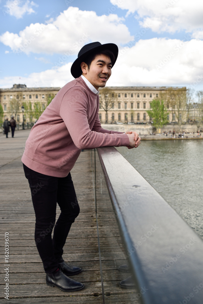 Paris,France -April 2,2017:  Young Good looking Asian man in pink shirt and black hat on Pont des Arts bridge  in Paris.