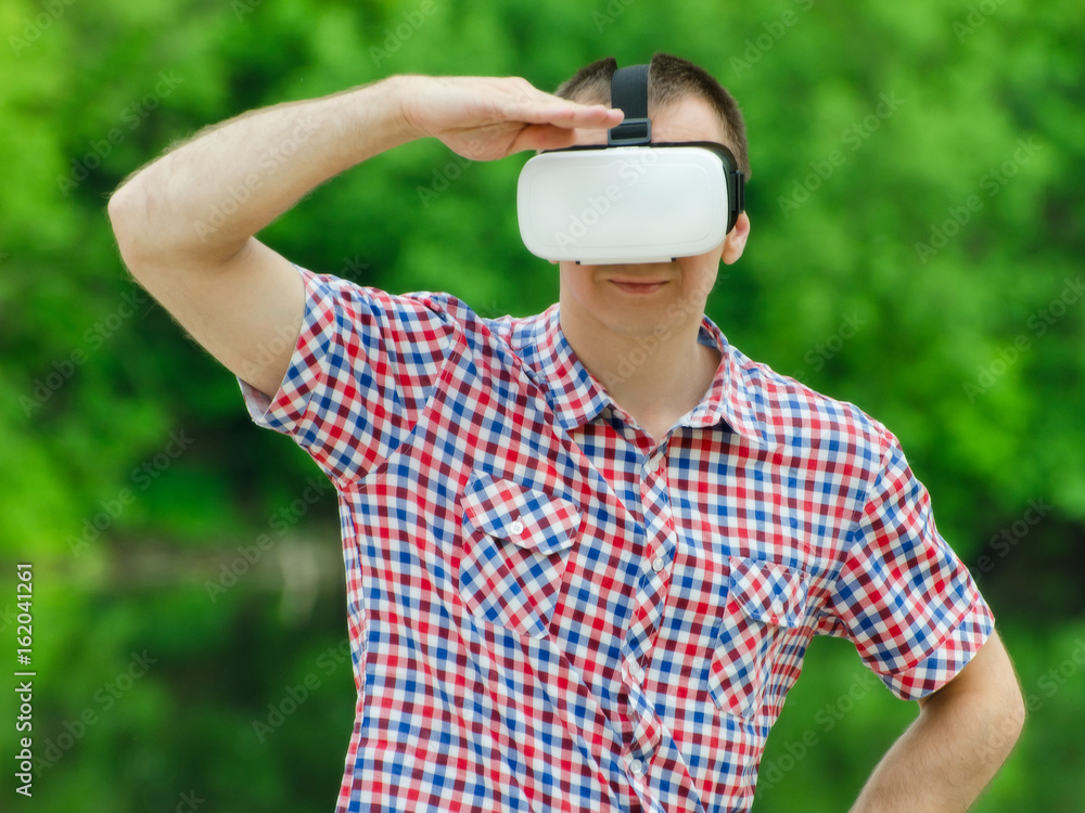 Man looks into the distance in the virtual reality glasses on background of green forest Man looks into the distance in the virtual reality glasses on background of green forest