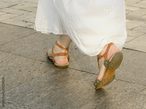 Feet walking on the sidewalk girl in a white dress and sandals