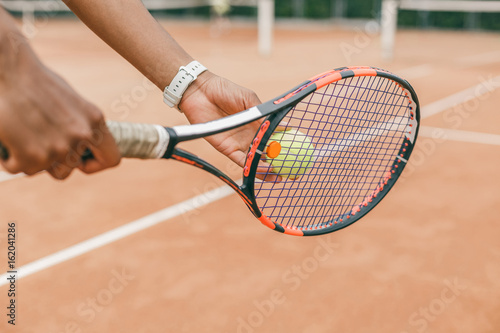 Close-up of male hand holding tennis ball and racket. Professional tennis player starting set. © belyjmishka