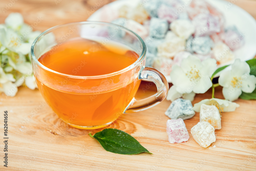Cup of green tea with jasmine decorated with a turkish delight on wooden table Cup of green tea with jasmine decorated with a turkish delight on wooden table