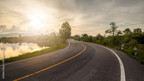 Windy road through forest and lake lead to sunrise photo
