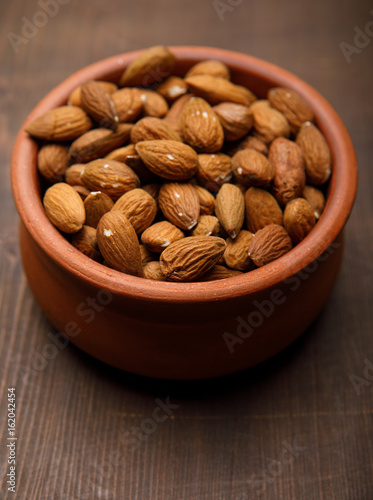 Almonds in a ceramics bowl against dark rustic wooden background