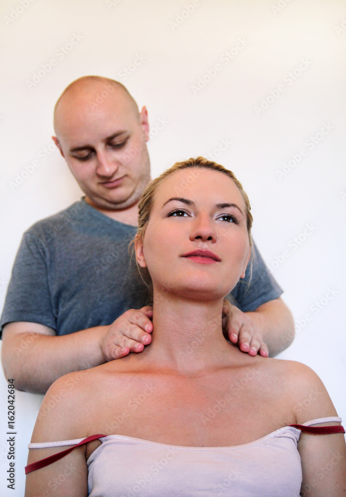Fototapeta premium Massage professional studio. Spa treatment. Man relaxing getting neck and shoulder massage. Masseuse human hands massaging for neck. Smiling woman sitting and having neck massage in medical office.