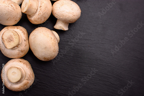 Whole mushrooms champignons whole lie on a black stone slate, background