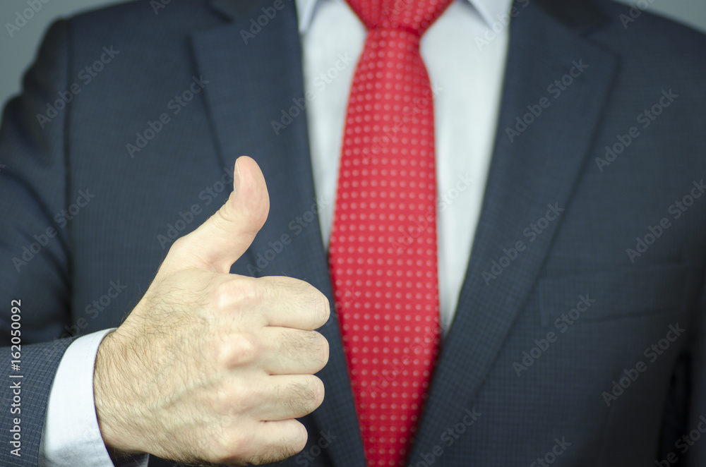A close-up view of a manager's hand in a suit and a red tie with thumb up A close-up view of a manager's hand in a suit and a red tie with thumb up