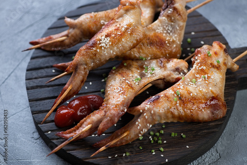 Black wooden serving board with barbecued chicken wings on skewers, studio shot, closeup