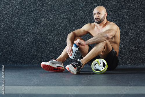 Shirtless man with bottle of water sitting on the floor of gym