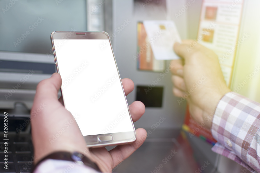 Hand of a man with a credit card, using an ATM. Man using an atm machine with his credit card. Closeup of male hands using smart phone while typing on ATM.
Hand of a man with a credit card, using an ATM. Man using an atm machine with his credit card. Closeup of male hands using smart phone while typing on ATM.
