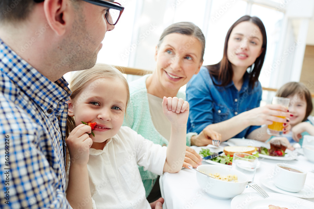 Cute girl eating fresh strawberry for breakfast with her family near by Cute girl eating fresh strawberry for breakfast with her family near by