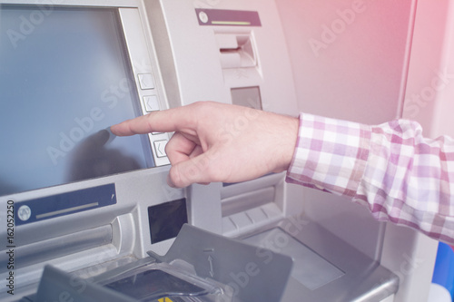 Hand of a man with a credit card, using an ATM. Man using an atm machine with his credit card. Closeup of male hands using smart phone while typing on ATM. 