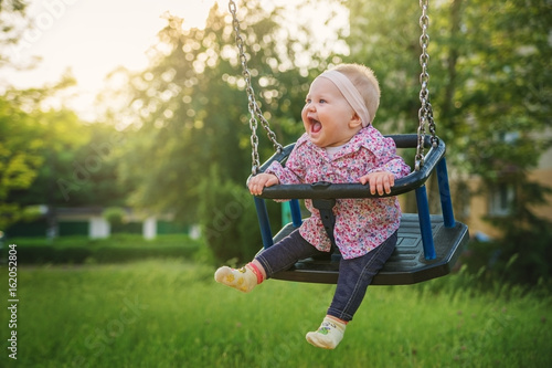 Shifting the little baby girl on swings on a summer evening.