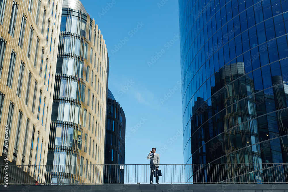Fototapeta premium Modern trader calling against blue sky between skyscrapers