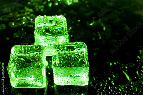 Green ice cubes on black wet table.