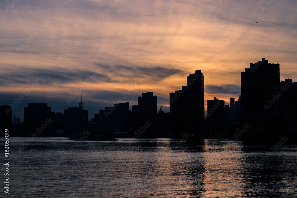 Silhouette of the Manhattan skyline at dusk. Colorful skies with strong contrast, reflections on the water surface
