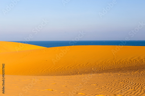 Yellow sandy wavy dunes with blue sea at background