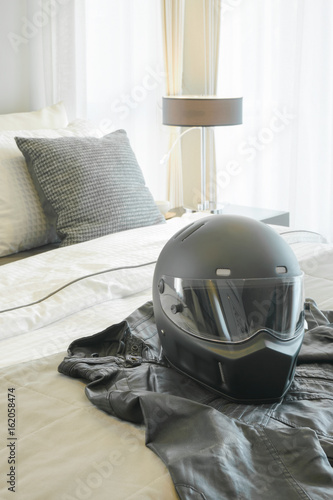 Motorcycle helmet and leather jacket setting on bed in modern bedroom