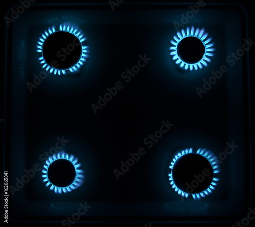 four burning gas stove hob blue flames close up in the dark on a black background top view