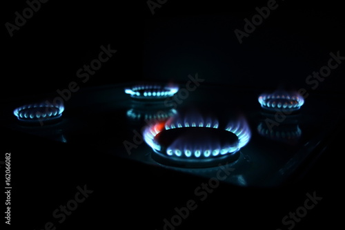 four burning gas stove hob blue flames close up in the dark on a black background