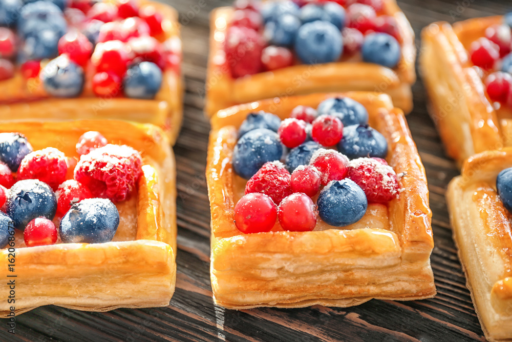 Delicious puff pastries with berries and sugar powder on wooden background Delicious puff pastries with berries and sugar powder on wooden background