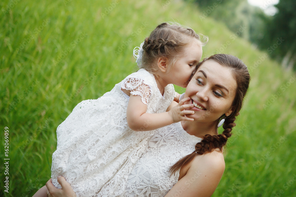 Young mother with daughter on hands in the same white dresses in the Park. Family Look Young mother with daughter on hands in the same white dresses in the Park. Family Look