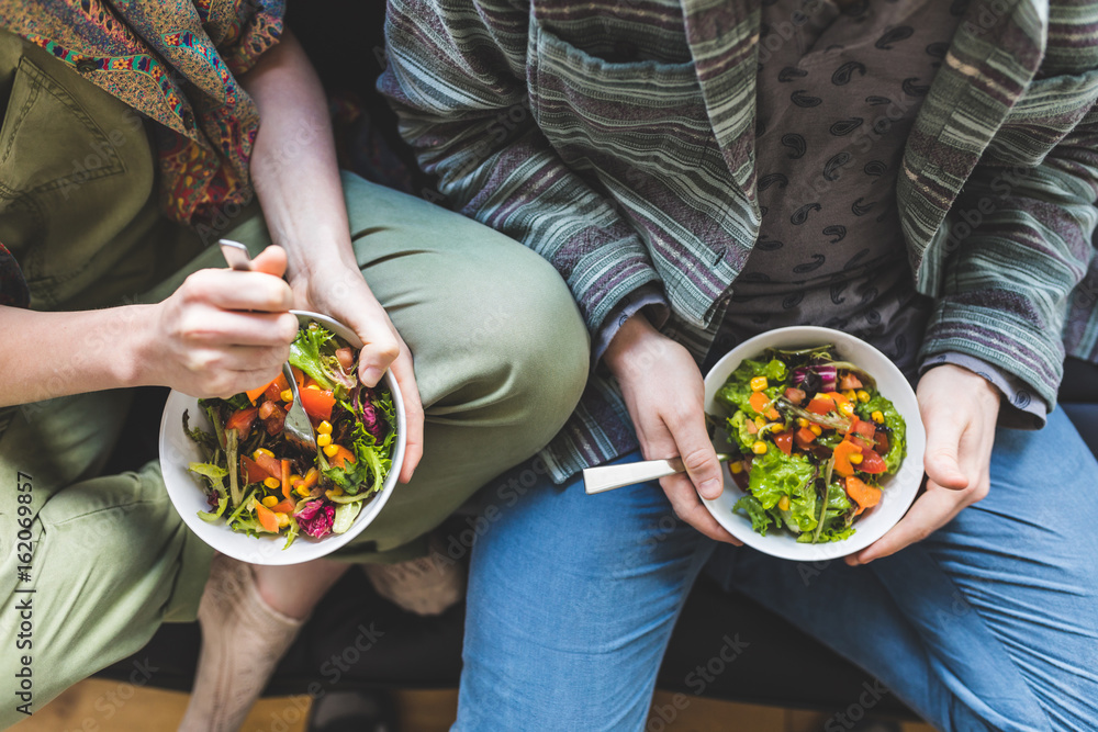 Couple eating healty salad at home on the sofa - obrazy, fototapety, plakaty 