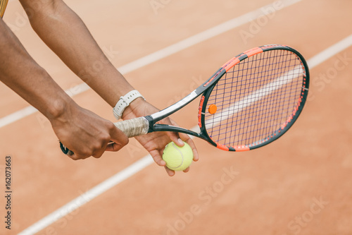 Close-up of male hand holding tennis ball and racket. Professional tennis player starting set. © belyjmishka