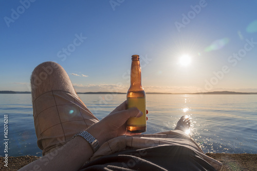 Personal perspective man laying down enjoying beer on the beach with setting sun photo