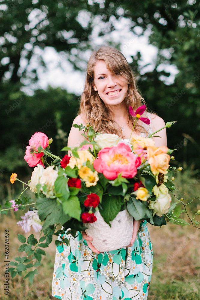 wedding, celebration, beauty, country life, spring, nature concept - young attractive woman with light brown hair in summer dress with floral print puting out nice bunch of various flowers wedding, celebration, beauty, country life, spring, nature concept - young attractive woman with light brown hair in summer dress with floral print puting out nice bunch of various flowers