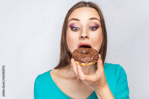 Portrait of beautiful girl with chocolate donuts. looking at donuts and trying to eat. studio shot on light gray background.