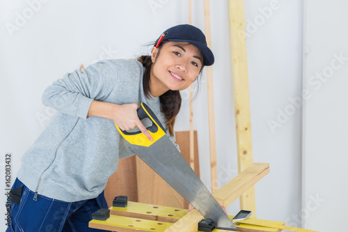 female carpenter sawing wood plank