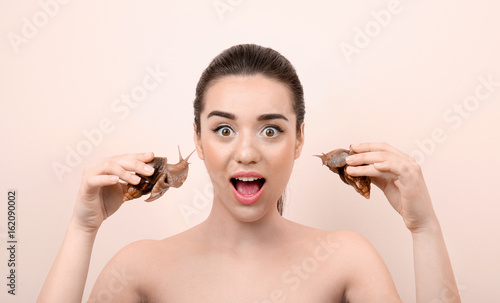 Beautiful young woman with giant Achatina snails on color background