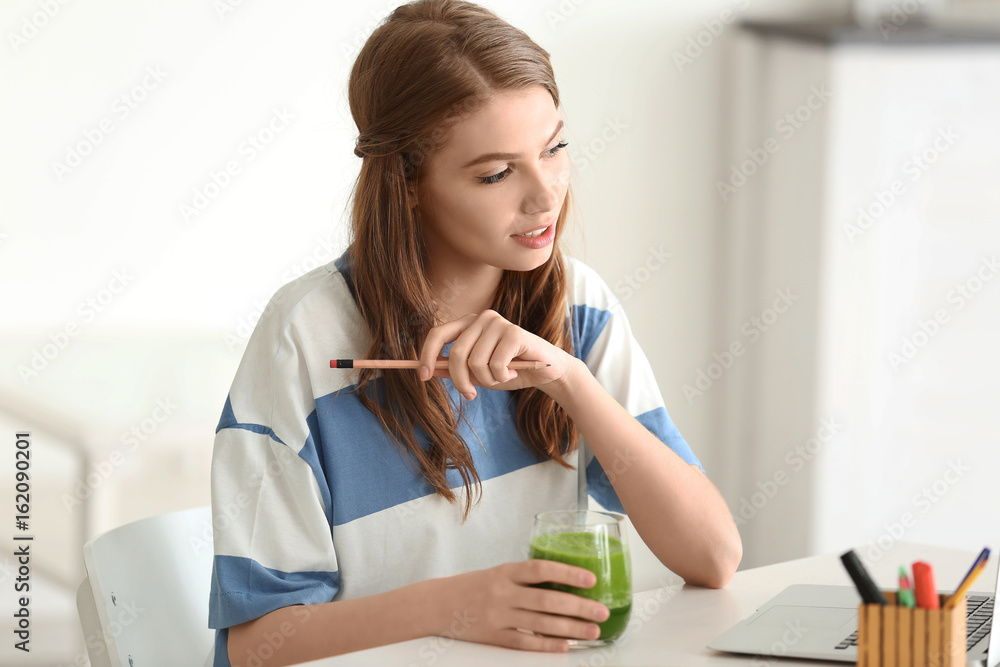 Weight loss concept. Beautiful young woman drinking healthy delicious smoothie and using laptop at home Weight loss concept. Beautiful young woman drinking healthy delicious smoothie and using laptop at home
