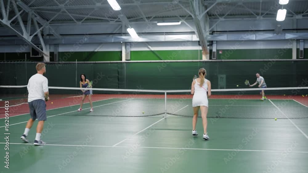 A company of friends play tennis on the sports ground, adult men and women throw a tennis ball on different sides of the field A company of friends play tennis on the sports ground, adult men and women throw a tennis ball on different sides of the field