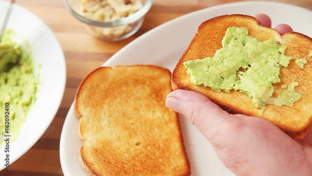 A man adds sliced almonds to avocado toast A man adds sliced almonds to avocado toast