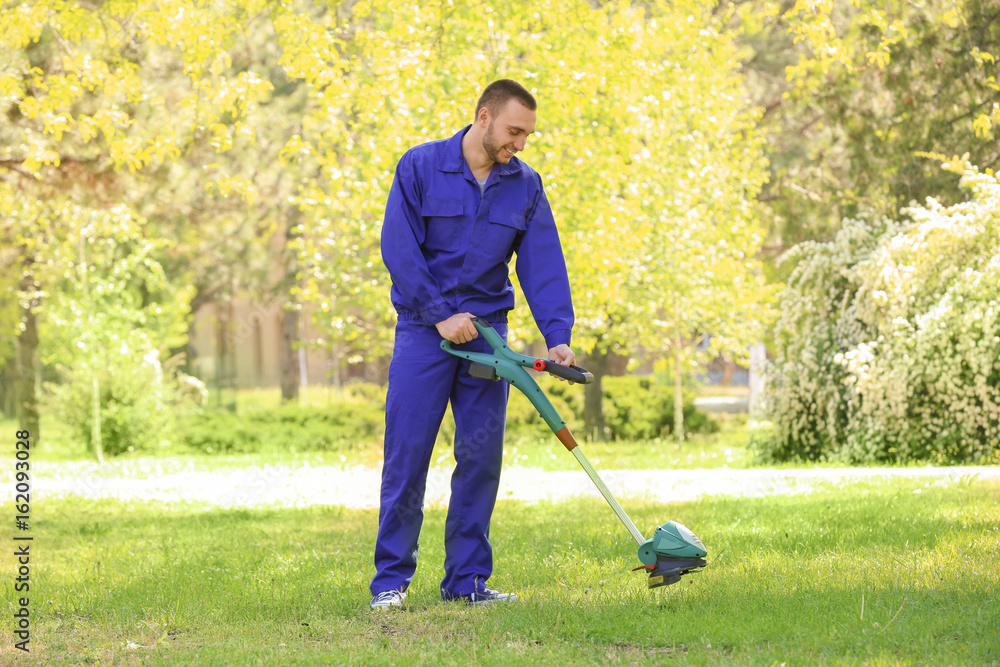 Young worker mowing lawn with grass trimmer outdoors on sunny day Young worker mowing lawn with grass trimmer outdoors on sunny day