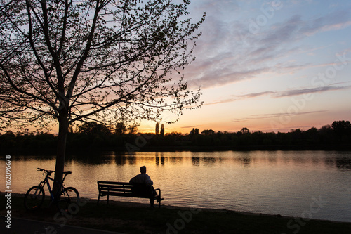 Man relaxing on a bench under a tree with beautiful sunset in background.