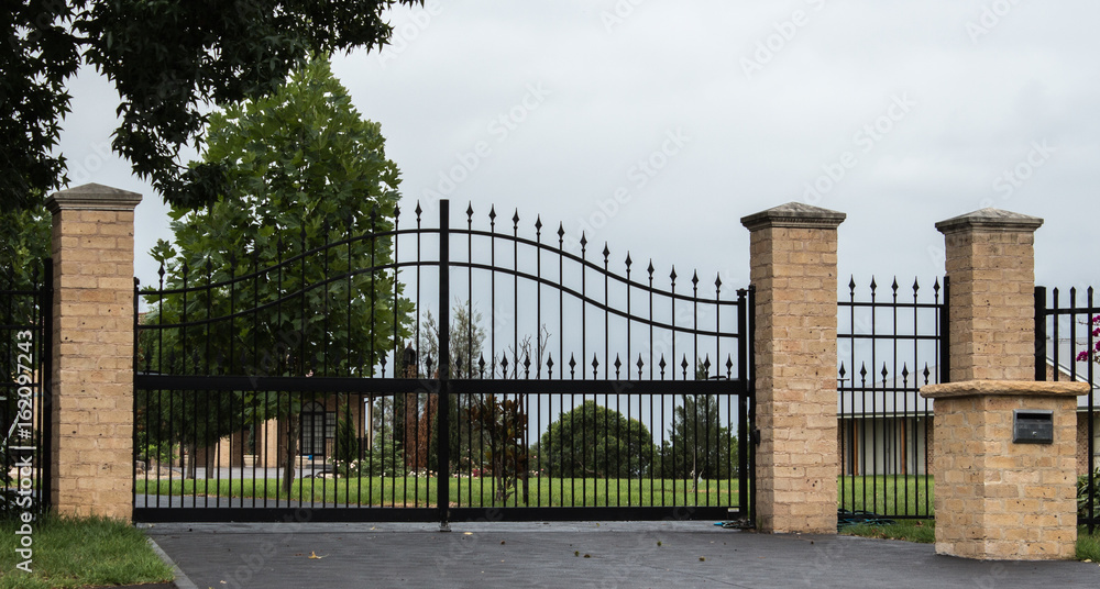 Black metal driveway entrance gates set in brick fence