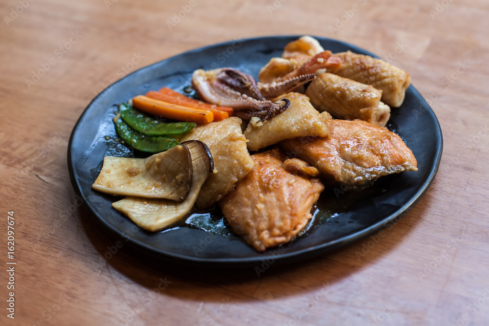 Seafood stire-fried with oil Japanese style cooking in the black disc on the wood table Seafood stire-fried with oil Japanese style cooking in the black disc on the wood table