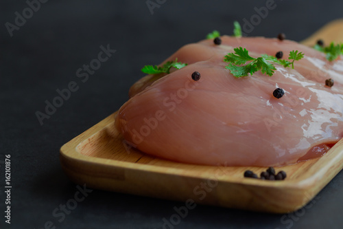 Chicken breat on wood plate sprinkle with black pepper and parsley. Slice raw chicken breast prepare for cooking. Preparation raw chicken breast put on black granite table for background or wallpeper.