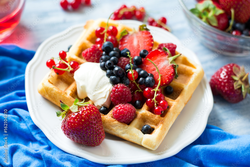 Healthy breakfast: Belgian waffles with sour cream, strawberry, raspberry, blueberry, cherry and red currant on blue wooden table. Selective focus Healthy breakfast: Belgian waffles with sour cream, strawberry, raspberry, blueberry, cherry and red currant on blue wooden table. Selective focus