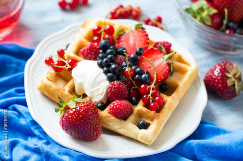 Healthy breakfast: Belgian waffles with sour cream, strawberry, raspberry, blueberry, cherry and red currant on blue wooden table. Selective focus