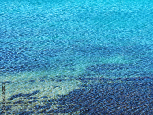 Turquoise blue background of an ocean space, view from above. Wavy sea surface. Kind of algae under water