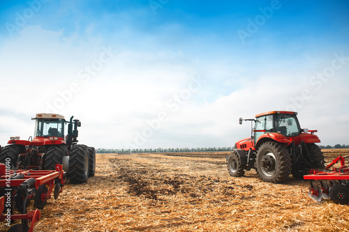 Two tractors with a plow in a field on a sunny day.