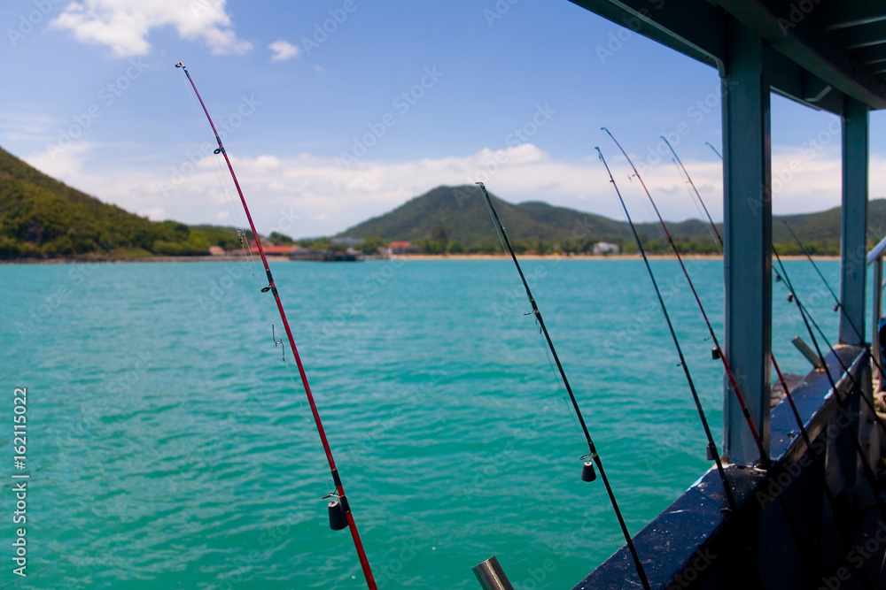 The fishing rods are leaning against the side of the ship against the background of the hilly coast.