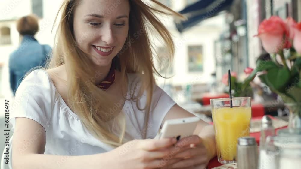 Pretty girl looks happy while texting on smartphone and drinking orange juice, steadycam shot
Pretty girl looks happy while texting on smartphone and drinking orange juice, steadycam shot