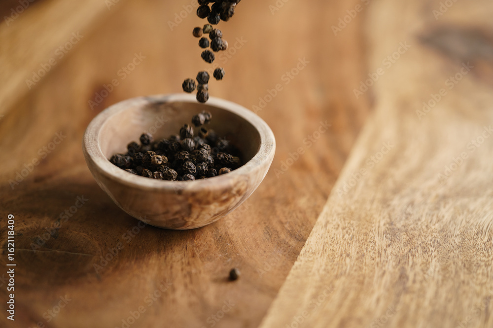 black dry pepper fall into wooden bowl on table black dry pepper fall into wooden bowl on table