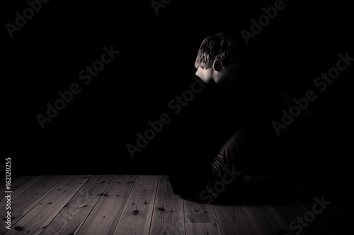 Young teenage boy sitting in darkness in an attic